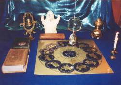 Auf dem mystischen Tisch sind Kristallkugel, Pendel, Kerze, Glocke, Feuerschale, Sternzeichen, alte Zauberbücher, eine Gespenster-Figur!